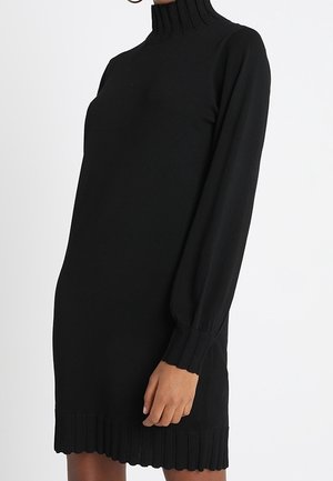 Robe en tricot noire avec col montant, manches longues à poignets côtelés, et ourlet côtelé avec un bord festonné. Texture lisse sur l'ensemble.