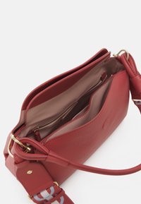 Czerwona skórzana torebka o teksturowanym wykończeniu, z zamknięciem na zamek błyskawiczny oraz dekoracyjnym paskiem z wzorem. Widok od środka pokazuje kieszenie.