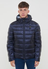 Giacca imbottita blu navy con cappuccio, texture lucida, chiusura con zip, tasche laterali e pannelli orizzontali cuciti. Design leggero e isolato.