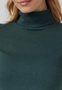 Donkergroen coltrui gemaakt van geribbeld materiaal, met een aansluitend ontwerp dat soepel de halslijn volgt.