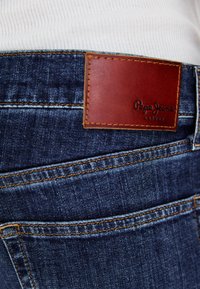 Traperice tamnoplave boje, s smešnim kožnim etiketom "Pepe Jeans London" i narančastim šavovima oko džepova.