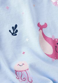 Un tejido azul claro presenta estampados juguetones de una ballena rosa, medusas, coral y estrellas en suaves colores pastel. Textura suave y diseño colorido.