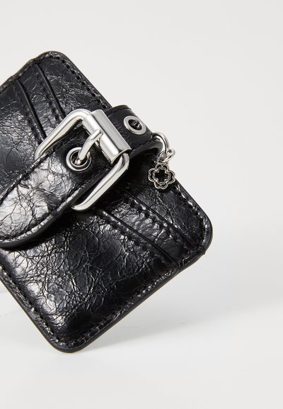 Portofel din piele neagră cu un finisaj texturat, hardware cu cataramă argintie, închidere prin buton, și detalii cu farmec, având sloturi pentru carduri și accente de cusătură.