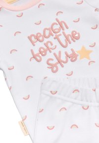 Conjunto de pijama blanco con un estampado de arcoíris en tonos de rosa, con la frase "apunta al cielo" en letras texturizadas de color rosa y un detalle de estrella naranja; suave tejido de algodón.