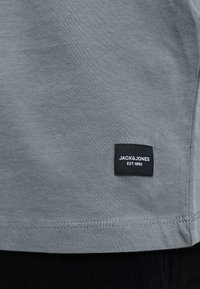 Gray fabric with a small black rectangular label reading "JACK & JONES EST. 1990" sewn near the bottom hem.