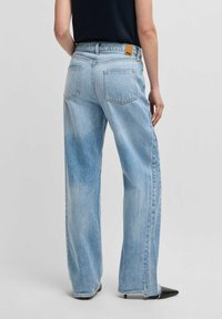 Ljust blå denimvidbenade jeans med hög midja, som har bakfickor i lapptyg, stickningsdetaljer och en brun läderlogotags.