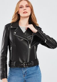 Zwarte leren motorjack met zilveren studs, asymmetrische ritsluiting en twee ritszakken. Voorzien van een ceintuurlint en reverskraag.