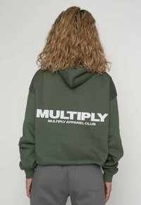 Groen sweatshirt met capuchon, voorzien van grote witte tekst op de achterkant: "MULTIPLY MULTIPLY APPAREL CLUB." Gemaakt van een katoenmix, casual pasvorm.