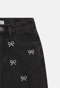 Juodos džinsinės kelnes su penkiais mažais cirkonių lankelių raštais šalia priekinio dešinio kišenės ir juosmens mygtuko uždarymu.