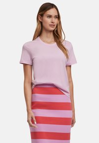 T-shirt rosa chiaro a maniche corte con scollatura rotonda, abbinato a una gonna a maglia a righe con strisce orizzontali alternate rosse e rosa.