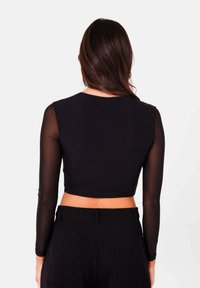 Top corto nero con maniche lunghe e trasparenti; tessuto morbido, scollatura rotonda e design aderente; abbinato a pantaloni neri a vita alta.