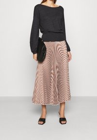 Black long-sleeve top paired with a patterned, pleated skirt in beige and rust tones; sleek black handbag and open-toe black heels.