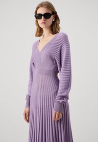 Robe à manches longues, décolleté en V de couleur violet clair, avec une texture côtelée et un design plissé, dotée d'une taille ceinturée et de poignets texturés.
