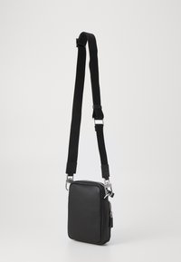Sac bandoulière noir en matériau texturé, avec une fermeture éclair, une sangle réglable et des accents en métal. Forme carrée.