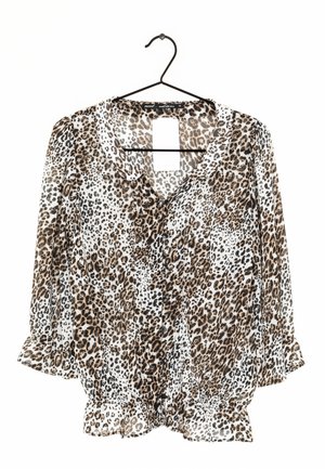 Blouse à manches longues imprimée léopard avec poignets et ourlet à volants, boutonnée devant avec un petit col, suspendue sur un cintre noir sur fond blanc.