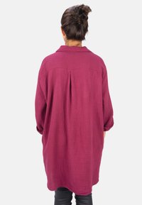 Oversized burgundy shirt with a textured fabric, featuring a spread collar, pleat detail at the back, and rolled sleeves.