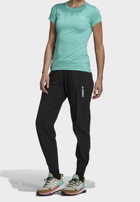 Camiseta ajustada de color turquesa claro, pantalones elásticos negros con logo blanco y zapatillas deportivas multicolores, con material transpirable y diseño deportivo.