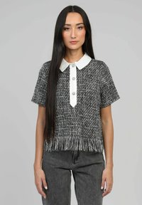 T-shirt à manches courtes en tweed noir et blanc avec ourlet à franges. Il présente un col blanc et une fermeture à boutons à l'avant avec des boutons décoratifs.
