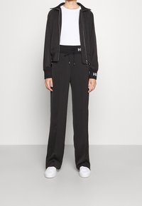 Giacca nera con zip e polsini a coste, abbinata a pantaloni neri a vita alta. Entrambi realizzati in materiale elasticizzato. Scarpe da ginnastica bianche completano l'outfit.