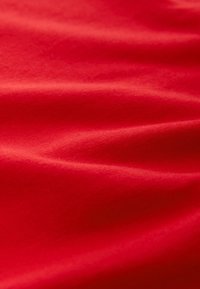 Tissu rouge lisse avec des plis doux et une surface légèrement brillante qui reflète la lumière de façon uniforme.