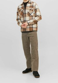 Bruin en crème geruit flanellen overhemd met twee borstzakken, gecombineerd met bruine rechte broek en zwarte schoenen, op een neutrale achtergrond.