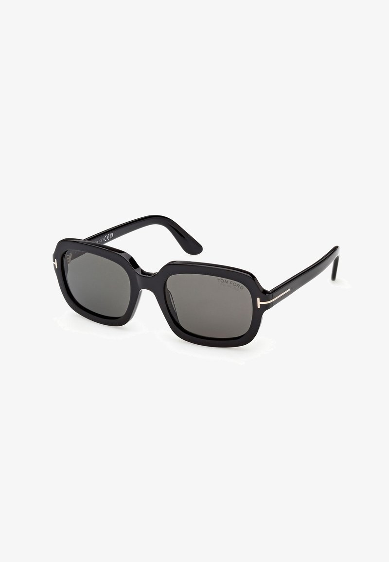 Lunettes de soleil à monture carrée noire avec verres foncés et accents subtils en forme de T dorés sur les branches, marquées "Tom Ford" sur le verre.