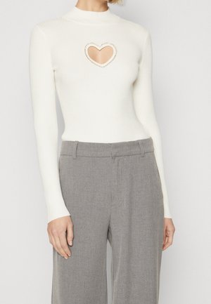Haut blanc à manches longues côtelé avec une découpe en forme de cœur au niveau de la poitrine, associé à un pantalon gris taille haute et ajusté.