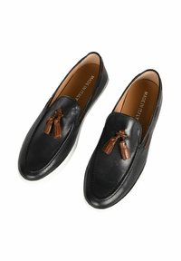 Mocassini in pelle nera con dettagli in frange marroni e suole in gomma bianca. Texture liscia, design arrotondato e dettagli di cucitura sui bordi.