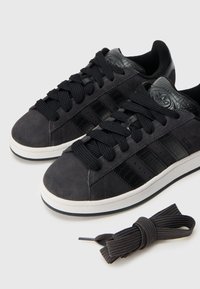 Čierne semišové tenisky s textúrovanými čiernymi akcentmi, okrúhlymi šnúrkami a bielou gumovou podrážkou. Súčasťou balenia sú aj extra čierne šnúrky.