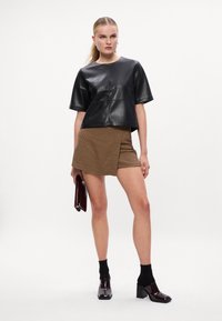 T-shirt de couro preto de mangas curtas com decote redondo, acompanhado de uma saia mini xadrez castanha, meias pretas e sapatos de bloco brilhantes castanhos.