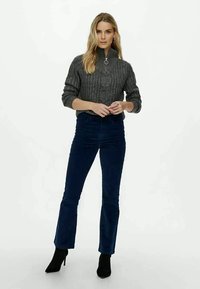 Γκρίζα πλεχτή ζακέτα με ψηλό γιακά, συνδυασμένη με σκούρο μπλε καμπάνα από κοτλέ παντελόνι και μαύρες μπότες μέχρι τον αστράγαλο. Απλά αξεσουάρ κοσμήματος.