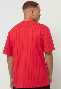 T-shirt en coton rouge à manches courtes, avec des rayures verticales noires et un col rond. Le dos est uni avec une coupe décontractée.