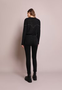Un pull en laine noire avec des détails cloutés dans le dos, associé à un pantalon skinny noir et des bottines noires. Texture lisse et coupe ajustée.
