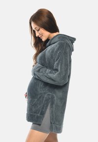 Fleece-Schwangerschafts-Hoodie in Dunkelgrau. Ausgestattet mit einer Kapuze, Seitentaschen und einem übergroßen Design mit strukturiertem Finish. Kurzärmel und Schlitze an den Seiten.