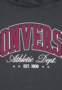 Felpa grigia con lettering bold in color marrone-burgundy che recita "CONVERS", con "Athletic Dept." e "EST. 1908" in bianco. Texture morbida in cotone.