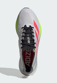 Grauer Sportschuh mit strukturiertem Obermaterial, schwarzen Schnürsenkeln, neongrüner Sohle und roten Akzenten. Verfügt über "ADIZERO" Branding im Inneren.