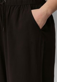 Zwarte broek met een gladde textuur, voorzien van zijzakken en een elastische tailleband met een trekkoord voor een verstelbare pasvorm.