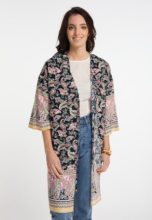 Zwarte paisley kimono met roze en groene bloemenpatronen, losse mouwen en een gouden accentrand. Gecombineerd met een witte top en jeans.