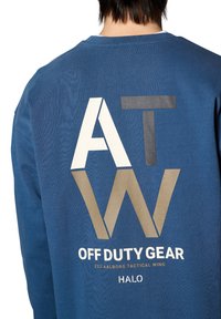 Niebieska bluza z dużą grafiką z tyłu, na której widnieją litery "ATW" w różnych kolorach, a poniżej znajduje się napis "OFF DUTY GEAR" w białym kolorze.