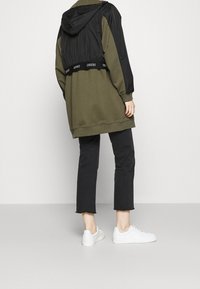 Huppari, jossa on musta yläosa ja oliivivihreä alaosa, sekä ribbausmustalla vyötärönauhalla. Yhdistetty mustien lyhyiden farkkujen ja valkoisten lenkkareiden kanssa.