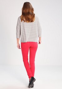 Blusa a rayas de manga tres cuartos en gris claro y blanco, combinada con pantalones rojos ajustados. Los detalles incluyen un corte relajado y una textura suave.
