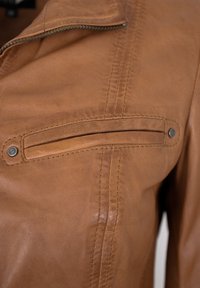 Braune Lederjacke mit glatter Textur, ausgestattet mit einer Reißverschlusstasche, Stickdetails und einem Druckknopfverschluss.