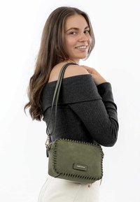 Borsa a tracolla verde oliva realizzata in materiale morbido, con bordi cuciti, chiusura con zip e tracolla staccabile.