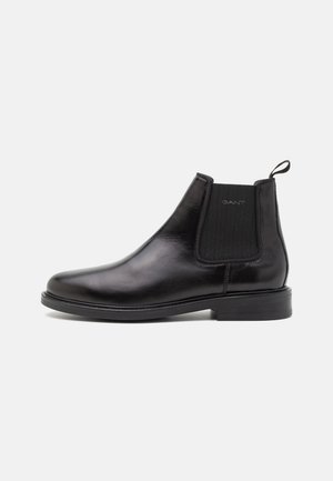 Black leather Chelsea boot featuring elastic side panels, a pull tab, smooth texture, rounded toe, and sturdy flat sole.