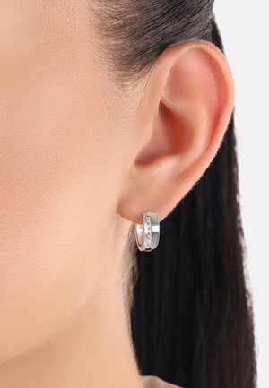 Pendientes de aro plateados con un acabado suave y una fila de pequeñas piedras transparentes en la parte frontal, sujetos al lóbulo de la oreja.