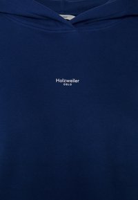 Felpa con cappuccio blu marino in tessuto morbido. Presenta una tasca a marsupio frontale e un cappuccio con coulisse. Scritta bianca con la dicitura "Holzweiler OSLO."