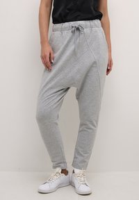 Svetlé šedé joggers so zúženým strihom vyrobené z mäkkej, ľahkej tkaniny s elastickým pásom a šnúrkou. Obsahuje bočné švy a manžety na spodnom okraji.