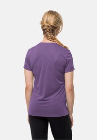 Purple short-sleeve t-shirt with a round neckline and smooth texture, worn with black pants, seen from the back.