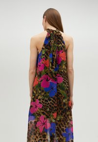 Vestido maxi con escote halter, patrones florales vibrantes en rosa, rojo y azul sobre un fondo de estampado de leopardo. La tela transparente cae con elegancia.