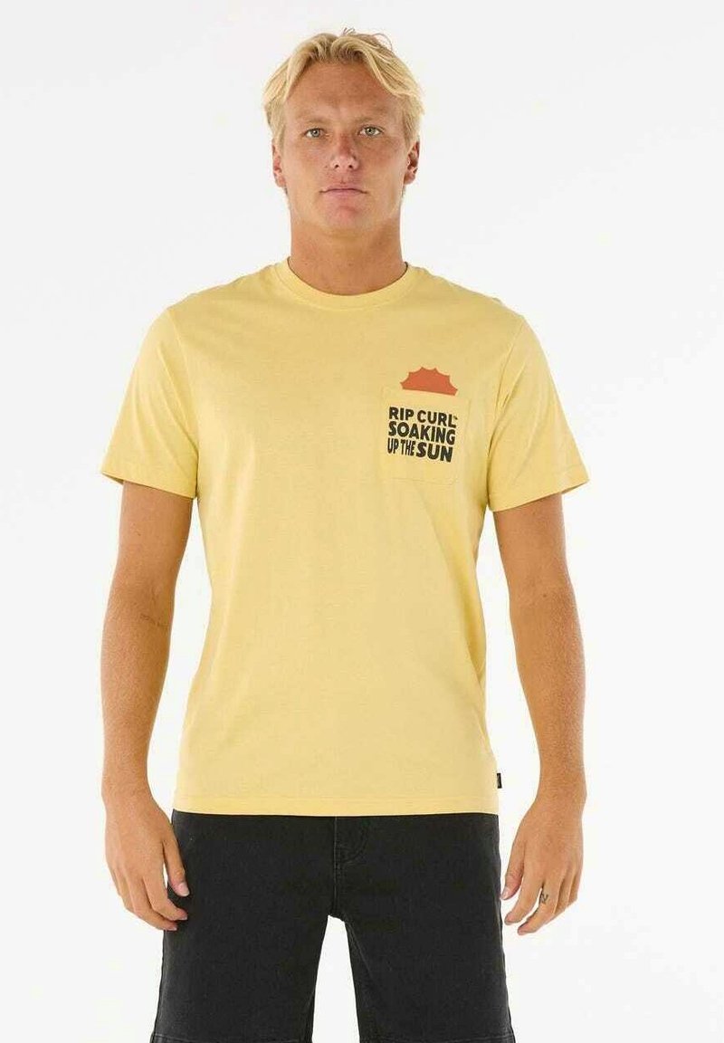 Gul t-shirt i bomuld med korte ærmer, rund halsudskæring og en lomme, der har orange detaljer og sort tekst, der står "RIP CURL SOAKING UP THE SUN."